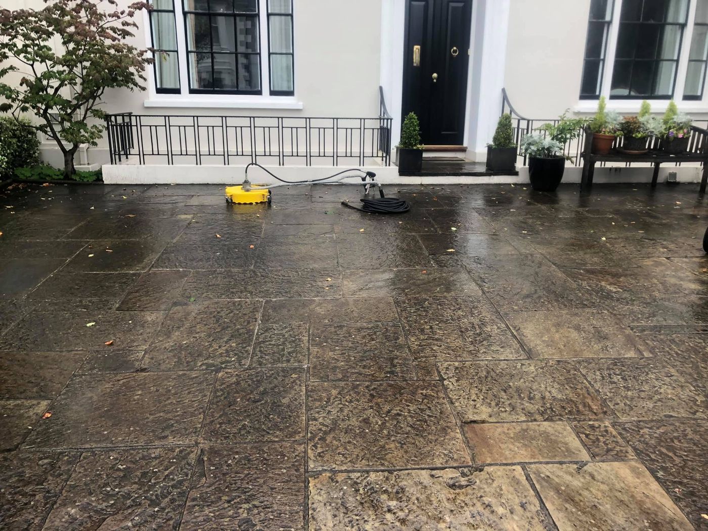 Patio and driveway before cleaning: dark, grimy paving with a surface cleaner at work